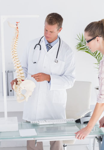 medical doctor pointing at a human spine while explaining it to a patient